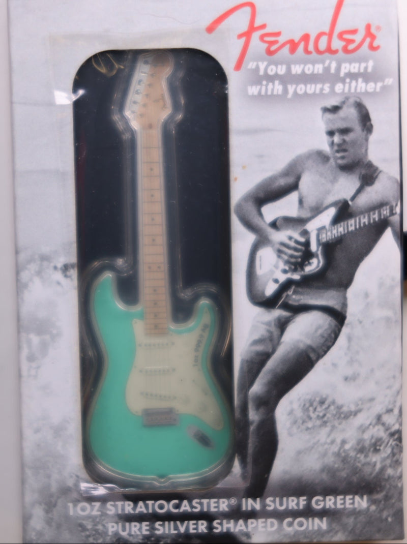 Fender Stratocaster-shaped silver coin in packaging with a black and white image of a man playing guitar.